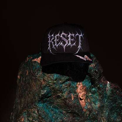 Black cap with 'RESET' logo on a textured green surface