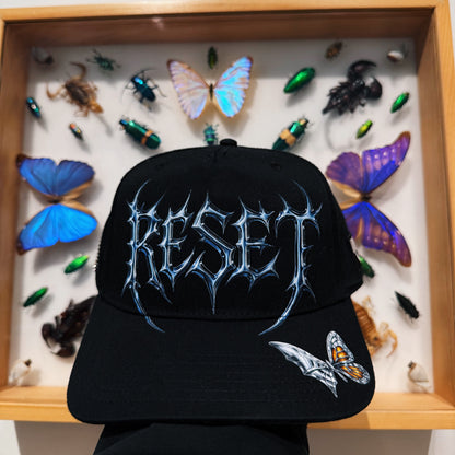Black cap with 'RESET' design in front of a display case with insects and butterflies.